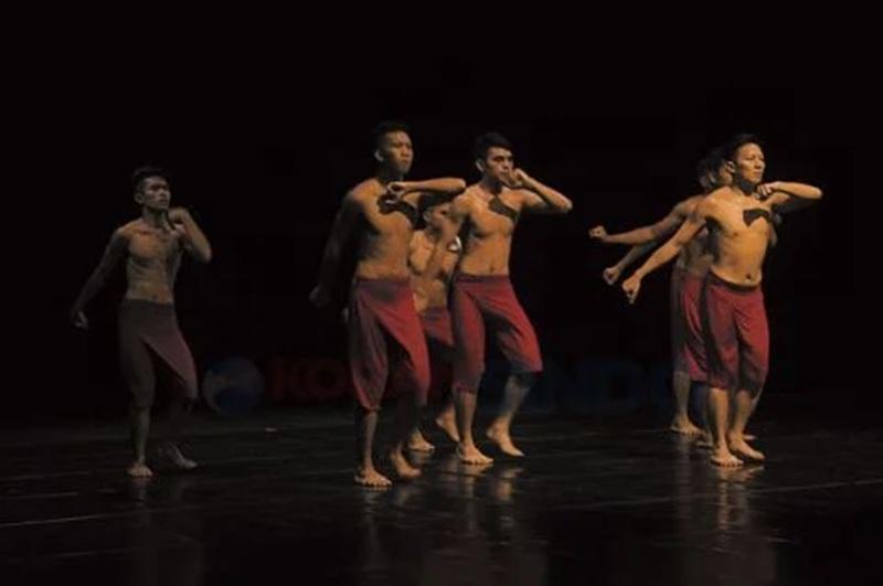 Five male dancers in red pants performing on dark stage