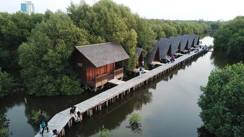 Wooden cabins and boardwalk over mangrove water with people