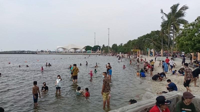 Crowded beach with people wading and palm trees