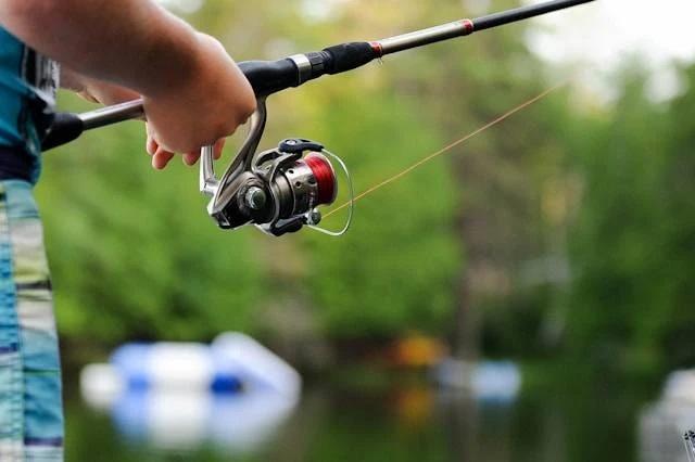 person holding spinning reel fishing rod over lake