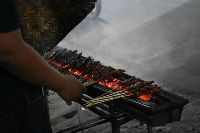 Person grilling satay skewers over charcoal