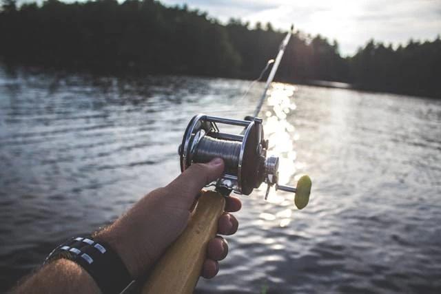 Person holding fishing reel over lake at sunset
