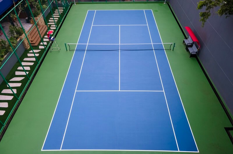 Aerial view of blue tennis court with green surroundings