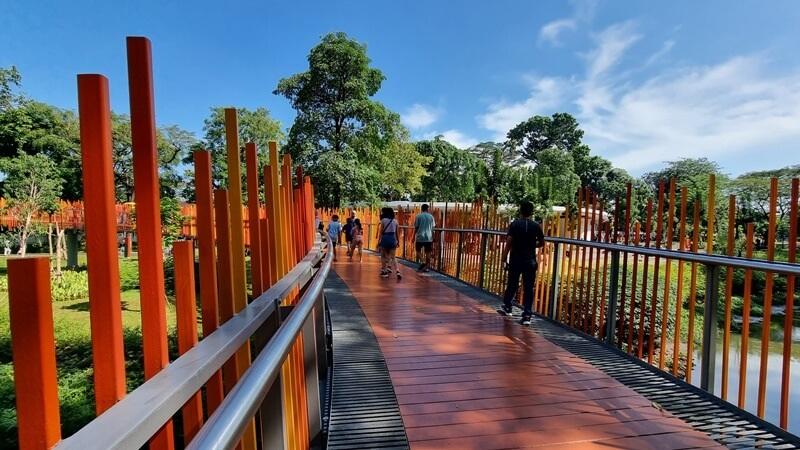 People walking on orange-posted boardwalk bridge in park