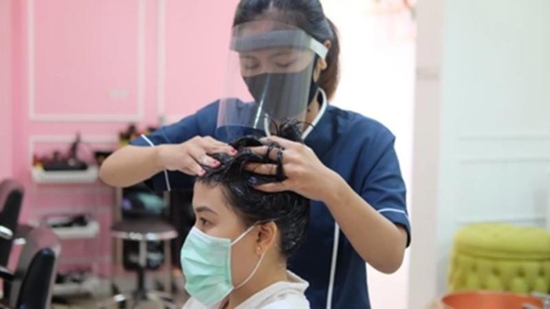 Hairdresser wearing face shield washing client's hair