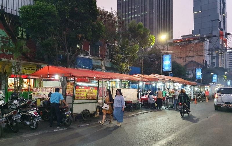 Outdoor street food stalls with people and motorcycles