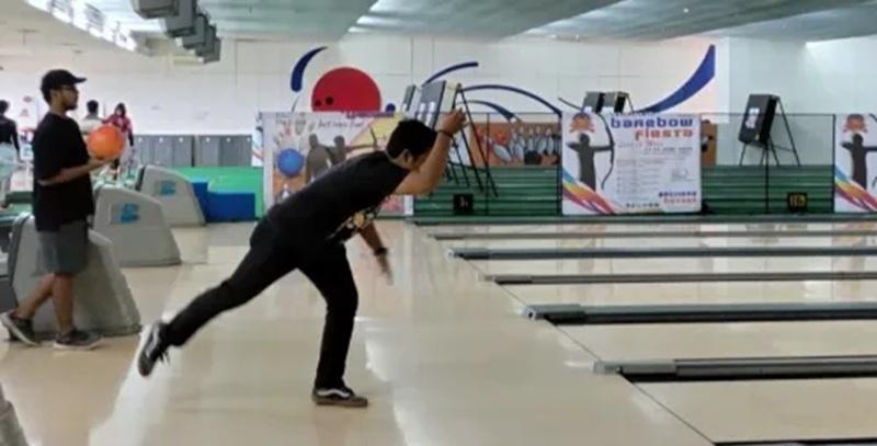 man releasing bowling ball down lane at bowling alley