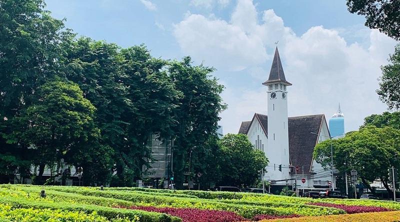 White church steeple by trees with colorful flowerbeds