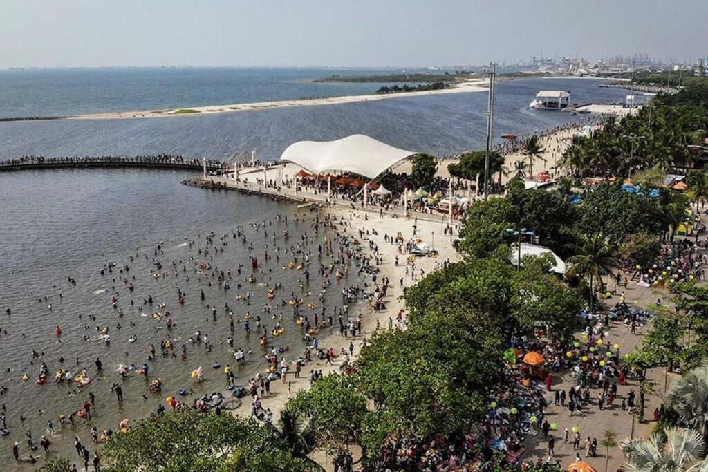 crowded beach park with white canopy and swimmers