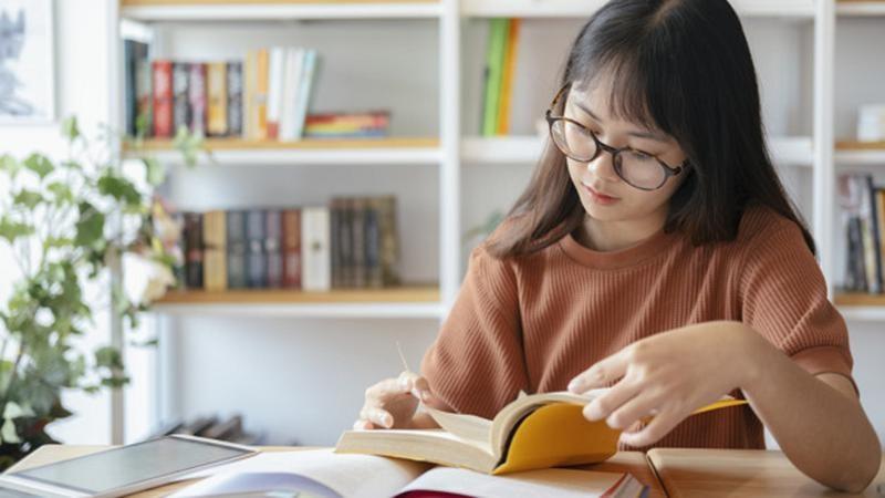 Student wearing glasses reading a book at a desk
