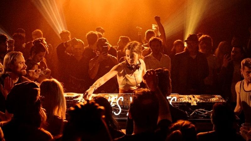 Female DJ playing to crowded orange-lit dancefloor