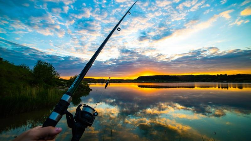Fishing rod over lake at sunset with sky reflections