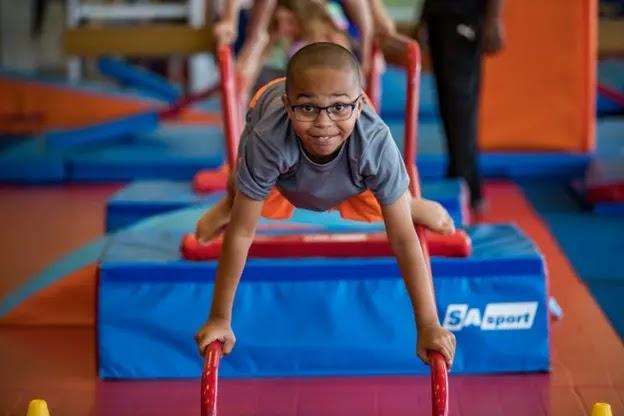 Smiling boy with glasses on gym obstacle bars
