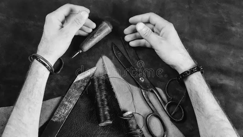 Hands working leather with scissors awl and thread