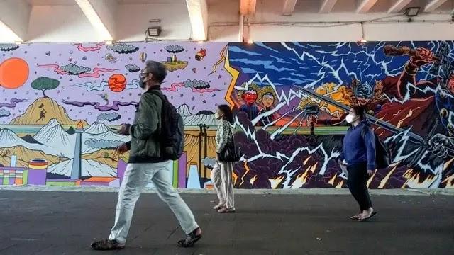 Three masked pedestrians walk past colorful mural