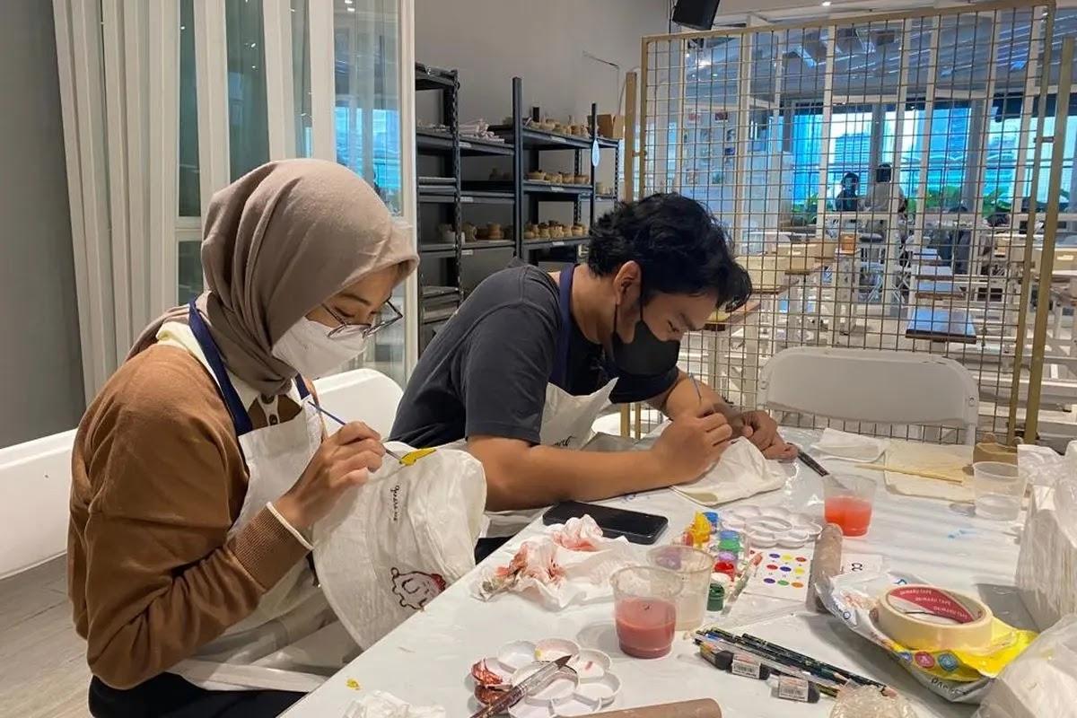 Two masked people painting ceramics at a craft table