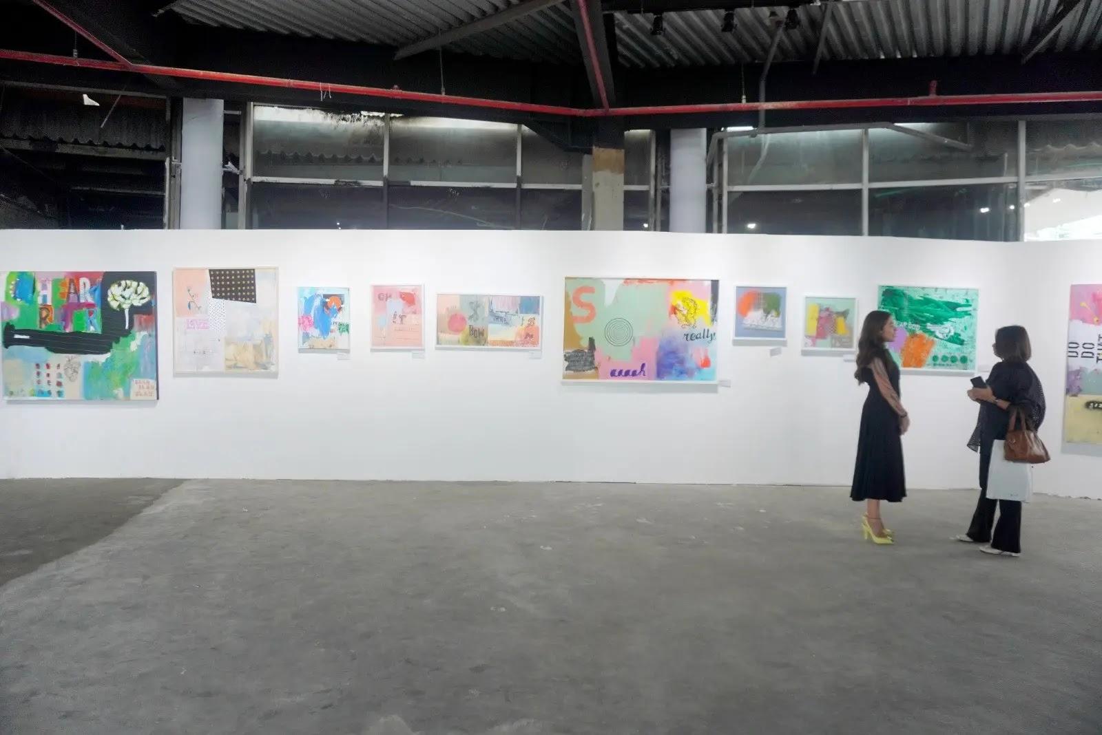 Two women viewing colorful paintings in an art gallery