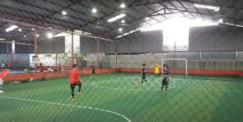 Indoor futsal match on green turf seen through netting