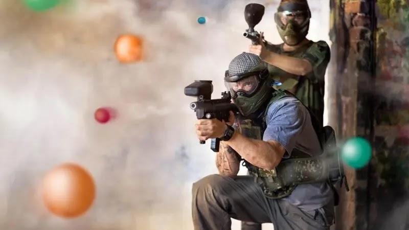 Two masked paintball players firing amid flying paintballs