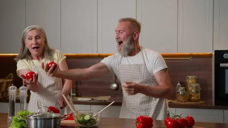 Elderly couple playfully tossing tomatoes while cooking