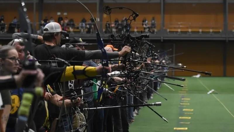 Archers lined up aiming compound bows indoors