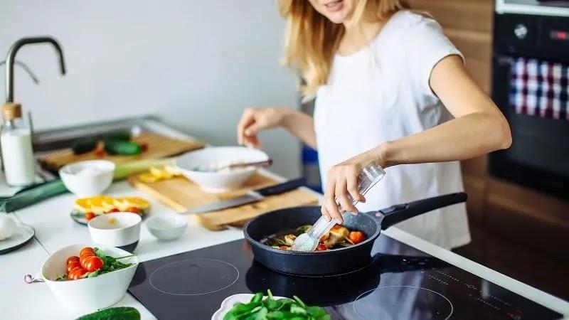 Woman stirring vegetables in a frying pan on stovetop