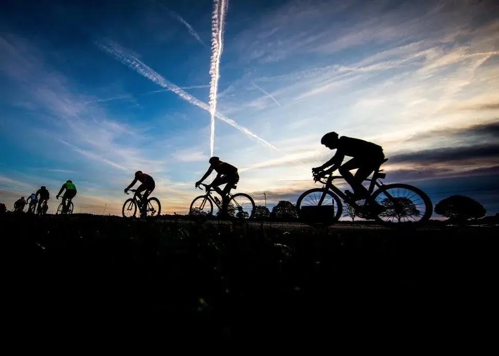 Cycling silhouettes at sunset with sky contrails