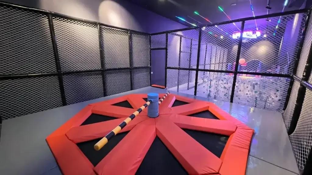 red padded jousting platform inside fenced indoor play arena