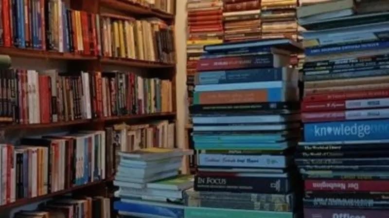 Stacks of books on shelves and piled on floor