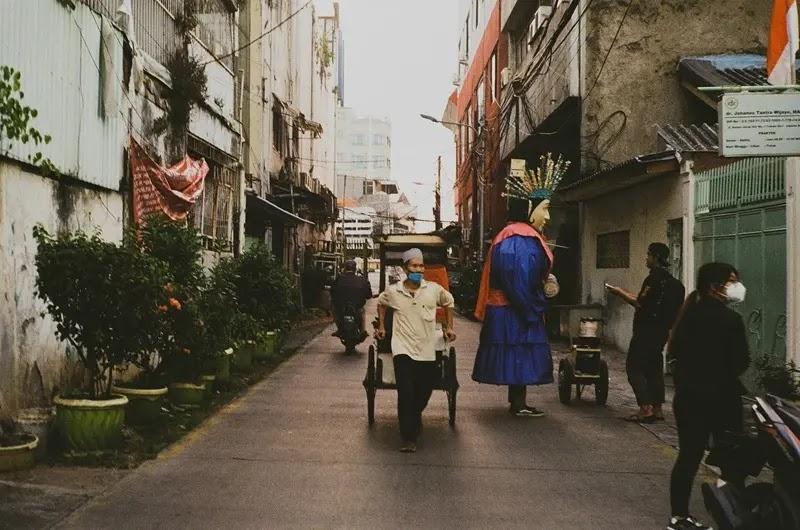 Street scene with masked rickshaw puller and giant puppet