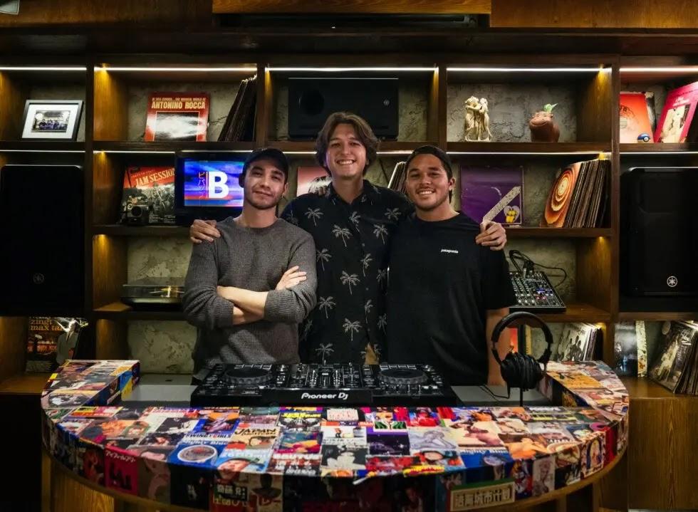 Three people smiling behind a colorful DJ booth