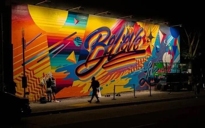 Night mural reading 'Believe' with artists painting