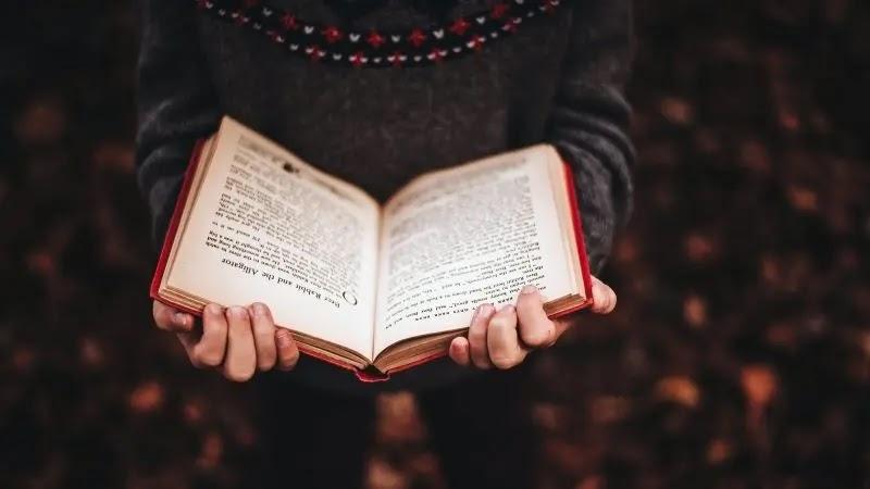 Hands holding open book with blurred autumn background
