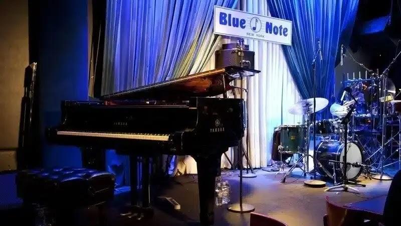 Blue Note logo above piano and drum set on stage