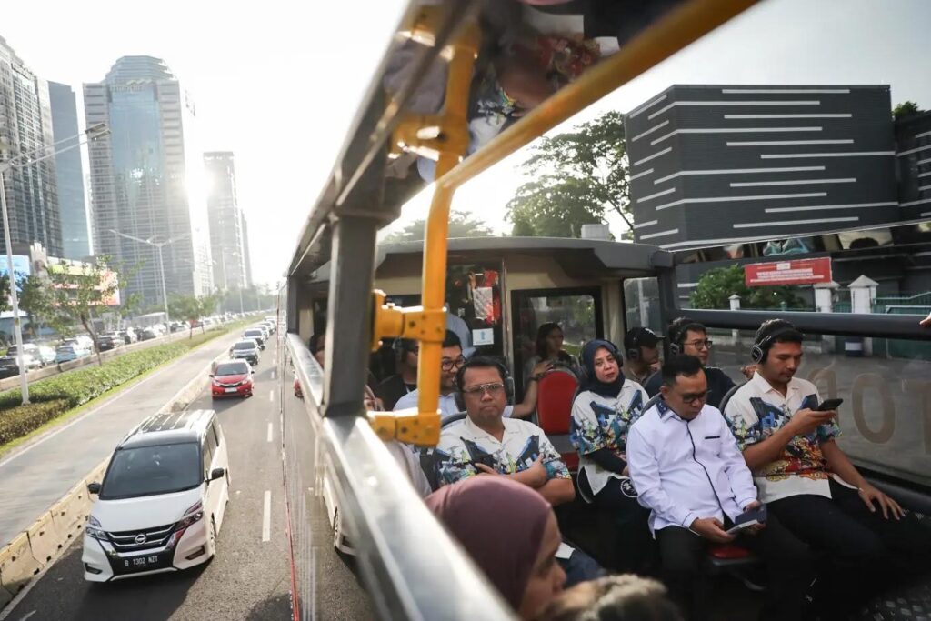 Passengers on open-top city tour bus wearing headphones