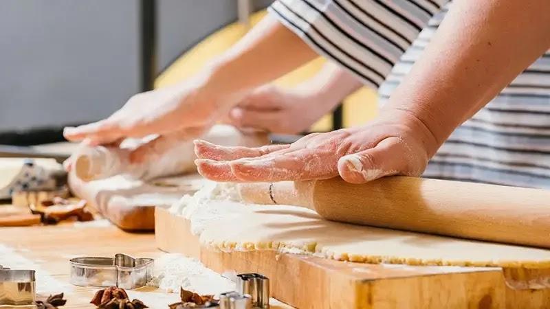 Hands rolling dough with rolling pin and cookie cutters