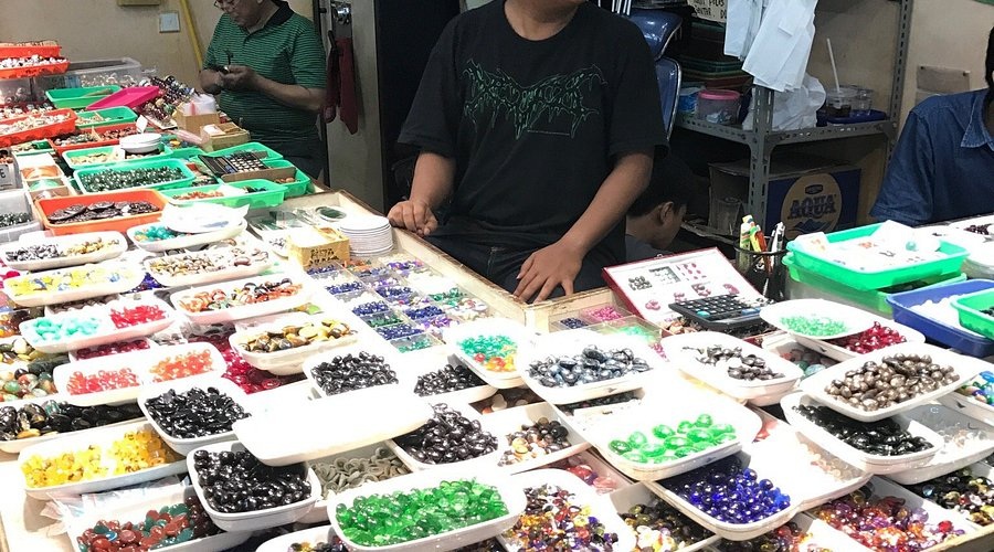 Busy craft table with rows of colorful beads and small jewelry components displayed on trays, workshop scene