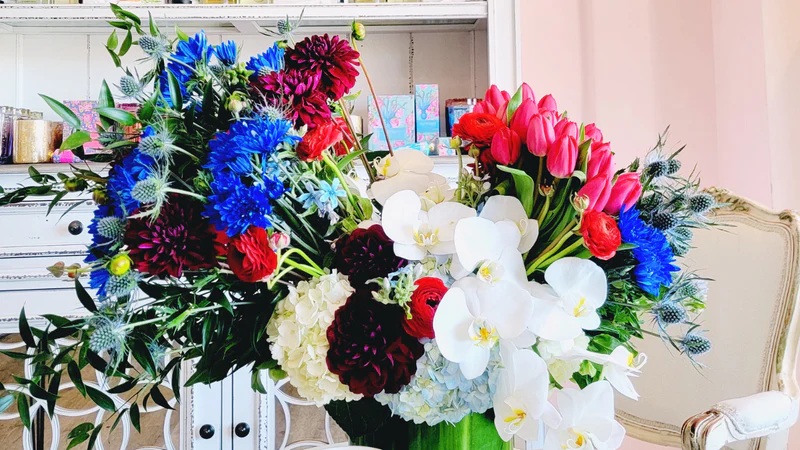 Colorful floral arrangement with blue, pink, red, and white flowers on an elegant sofa table indoors