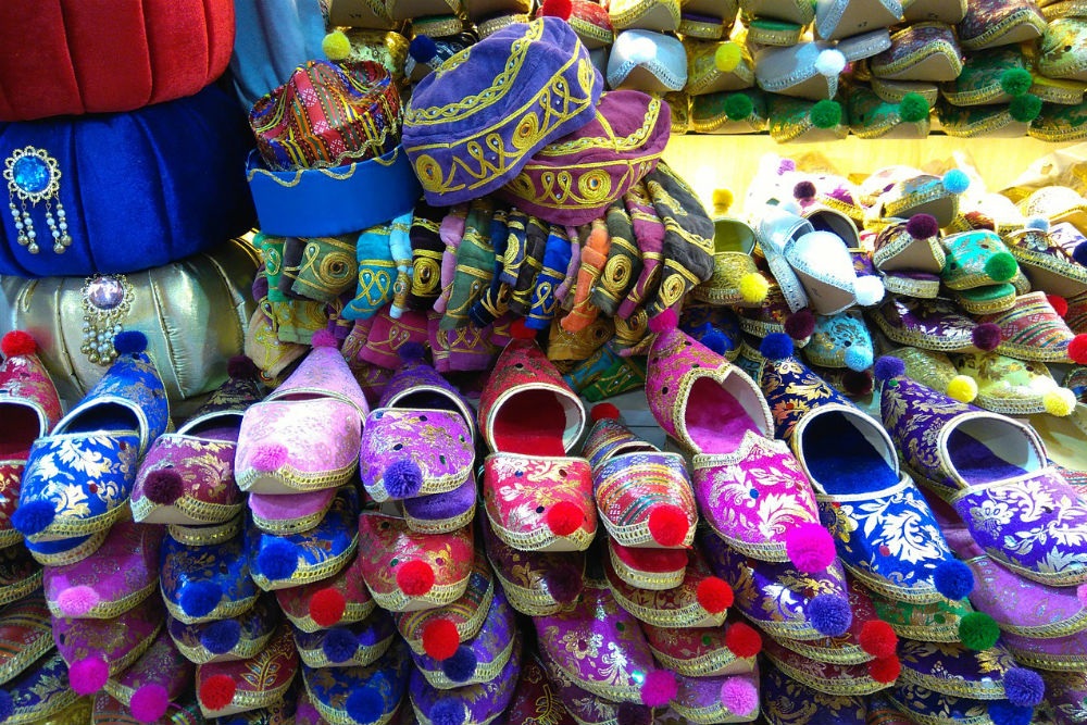 Colorful embroidered slippers with pom-poms in a market stall, blue and pink designs on display