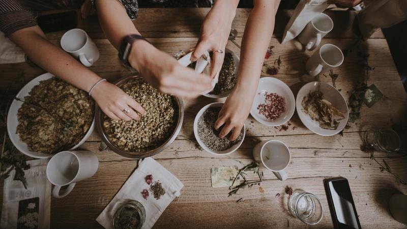 Hands pouring herbs and spices into bowls on a rustic wooden table during meal prep gathering