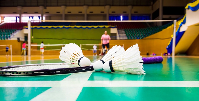 Badminton shuttlecock and racket on indoor court floor with players in background