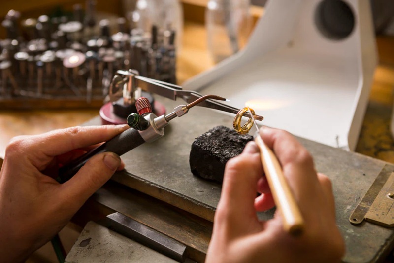 Jewelry making tools in use on a metal workbench, artisan holding tools and shaping a gold ring