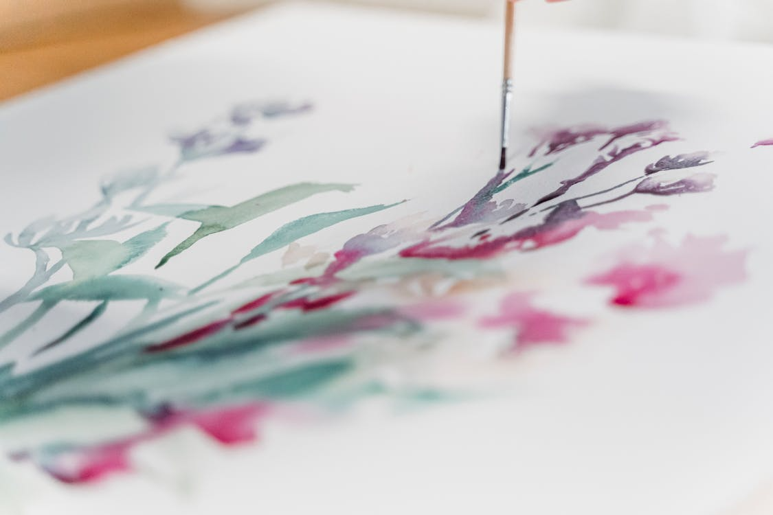 Close-up of paintbrush applying colorful watercolors on paper with magenta and teal strokes