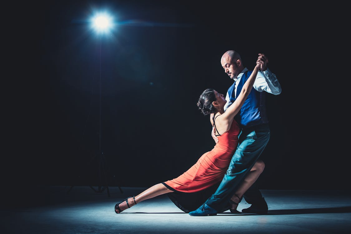 Dancing couple in blue and red clothing performing a dramatic stage pose under bright spotlight