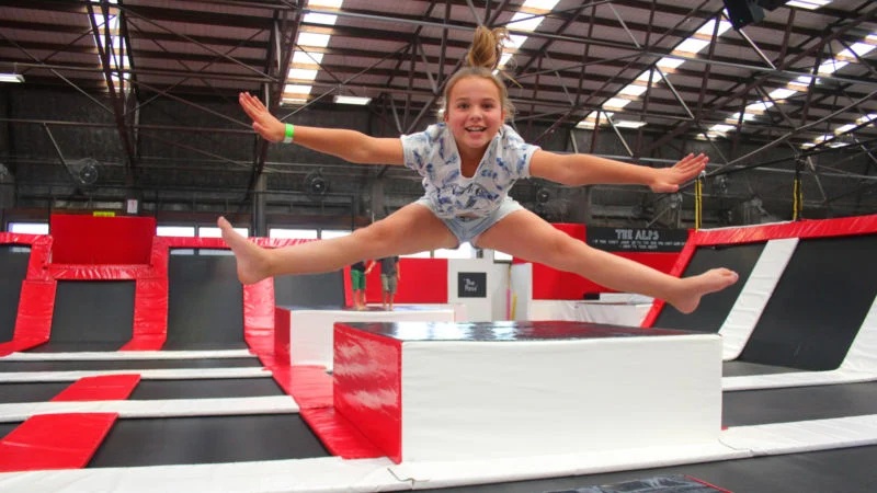 Young gymnast in a trampoline park performing a jump on a padded obstacle, arms outstretched