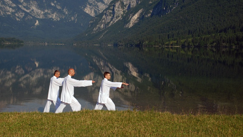 Three people in white walking outfits with arms outstretched by a calm lake and mountain reflection at sunrise