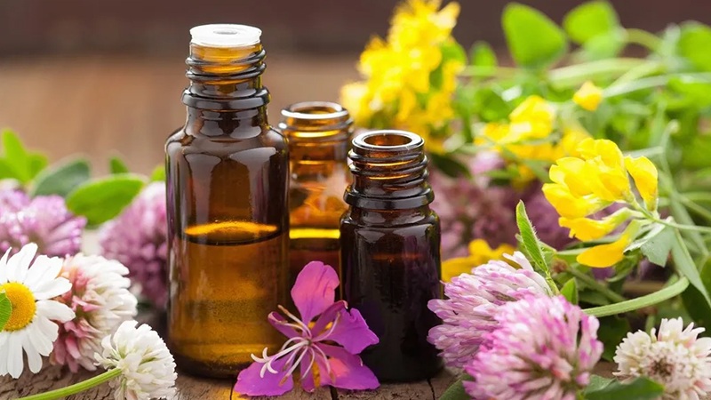 Essential oil bottles with droppers surrounded by colorful spring flowers and green leaves, outdoors on a wooden table
