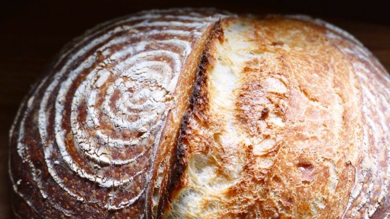 Sliced crusty sourdough bread loaf with swirled white and brown scoring, close-up on baked texture