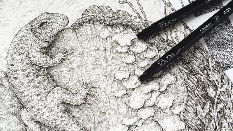 Black-and-white sketch of a lizard and hand with pen liner; makeup tools rest over the illustration