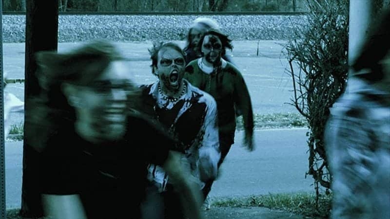 Zombie-like figures shamble along a dim walkway at night, one reaching toward the camera with eerie motion blur